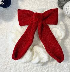 a knitted red bow sits on top of a white blanket next to crochet balls