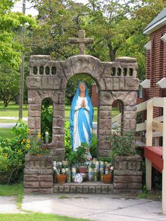 a statue of the virgin mary surrounded by plants and flowers in front of a building