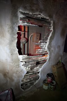 a hole in the wall that has been painted red and white with some paint cans next to it