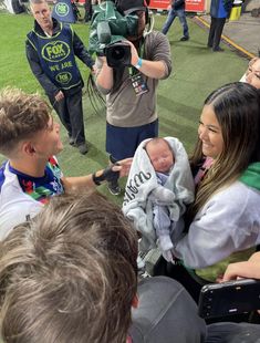 a group of people standing on top of a soccer field holding a baby in a blanket