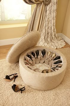 a round foot stool with many pairs of shoes in it on the floor next to a window