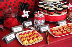 a red table topped with lots of desserts and candy covered plates on top of it