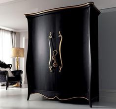 a black armoire with gold trim in a living room area next to a chair