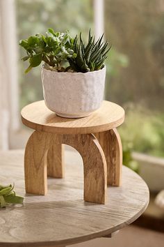 a small potted plant sitting on top of a wooden stool next to a window