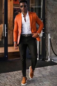 a man in an orange blazer and white shirt is walking down the street with his hands on his hips