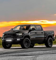 a black truck parked on the side of a road next to an orange and yellow sky