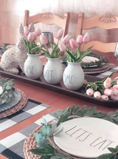 the table is set with pink tulips in vases