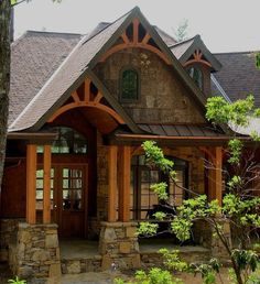 a stone house with wood trim around the front door and windows on both sides, surrounded by trees