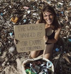 a woman sitting on the ground holding a sign that says, the world is changed by your example not your opinion