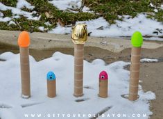 four decorated candles in the snow with one gold egg and two blue eggs on top