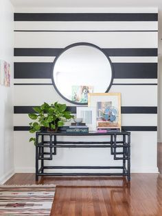 a black and white striped wall with a round mirror on the end table next to a potted plant