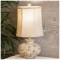 a white table lamp sitting on top of a dresser next to a potted plant