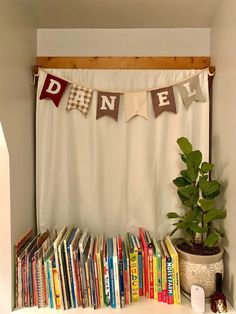 a bookshelf filled with lots of books next to a white curtain and potted plant