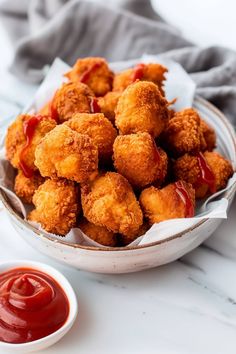 a bowl filled with fried food next to ketchup on a white counter top