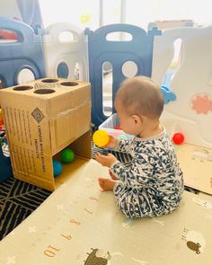 a baby sitting on the floor playing with some balls in front of a cardboard box