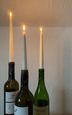 three wine bottles with candles in them sitting on a table