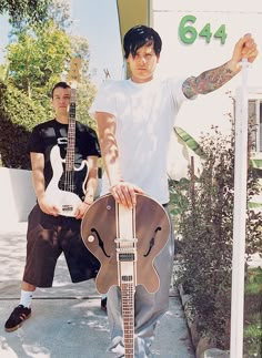 two men standing next to each other with guitars in front of them and one holding the guitar