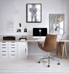 a desk with two computers on it in front of a white brick wall and wooden chairs