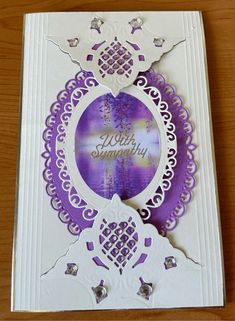 a purple and white greeting card with an ornate border around the edge, on a wooden surface