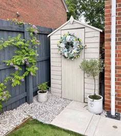 a small shed with a wreath on the door and two potted plants next to it