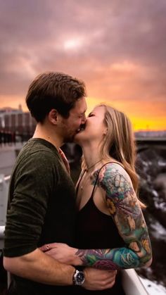 a man and woman kissing each other while the sun is setting