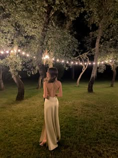 a woman standing in the grass at night with string lights strung across her back and trees behind her