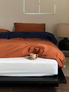 a bed with an orange and blue comforter on top of it next to a night stand