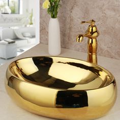 a bathroom sink that is shiny gold and has a vase with flowers in the background