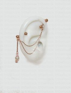 a white earring with two pearls and chains on it's side, hanging from a gold chain