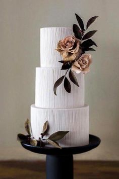 a three tiered white cake with flowers on top is sitting on a black plate