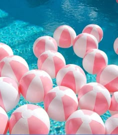 many pink and white beach balls floating in the water near a swimming pool with clear blue water