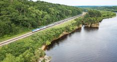 a train traveling over a bridge next to a river in the middle of a lush green forest