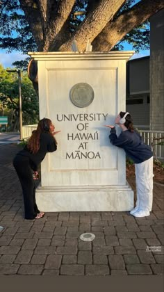 two women pointing at the university of hawaii sign