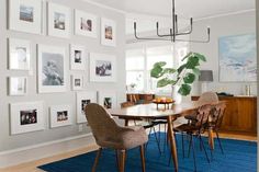 a dining room table with chairs and pictures on the wall behind it in front of a blue rug