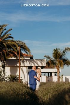 a man and woman standing next to each other in front of a building with palm trees