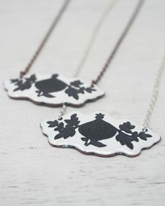 The Silhouette Necklace features a striking black and vintage pattern, fused onto white enamel. This piece brings historical charm into a modern context. Each necklace is crafted in small batches, ensuring a unique and sustainable accessory. Finished with 16-18" silver, copper, or sterling silver chain. Pendant measures approx. 1 3/4" by 3/4". Penny Jewelry, Silhouette Necklace, Sustainable Accessories, Vintage Revival, Vintage Silhouette, Floral Pendant, Upcycled Jewelry, Copper Chain, Enamel Jewelry