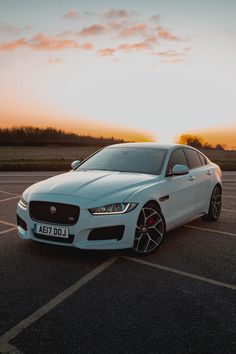 a white car parked in a parking lot with the sun going down on it's horizon