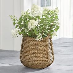 a wicker basket filled with white flowers sitting on top of a tile floor next to a window