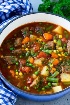 a bowl filled with stew and vegetables on top of a blue checkered cloth next to a spoon