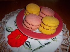 some pink and yellow cookies are on a red plate next to a white doily