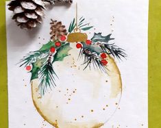 a watercolor painting of a christmas ornament with pine cones and holly berries