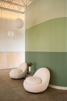 two white chairs sitting next to each other in front of a green and white wall