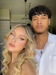 a man standing next to a blonde woman in a white shirt and black curly hair