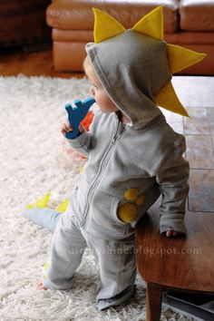 a toddler is sitting on the floor with a toy in his mouth and wearing a pikachu costume