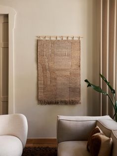 a living room with two white chairs and a rug on the wall in front of it