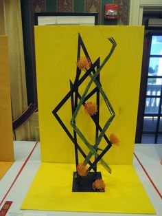 a piece of art made out of sticks and flowers on a yellow tablecloth covered table