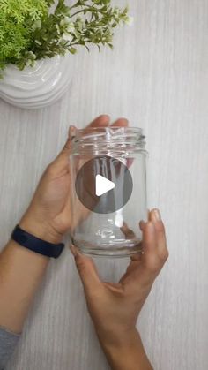 two hands holding a glass jar on top of a table next to a potted plant