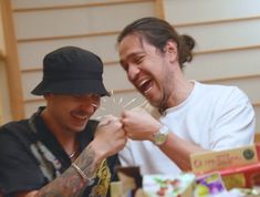 two men laugh as they hold sparklers in front of their faces while sitting at a table