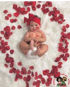 a baby is sitting on a white rug with red petals around it and her hands are in the air