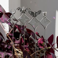 three metal sculptures sitting on top of purple plants